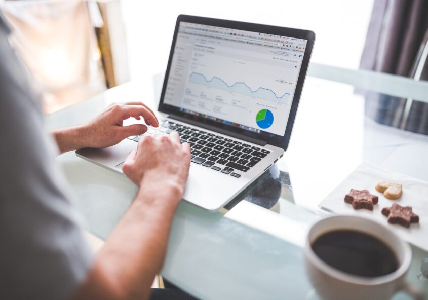 Person looking at analytics on a laptop screen at table with a cup of coffee and cookies.