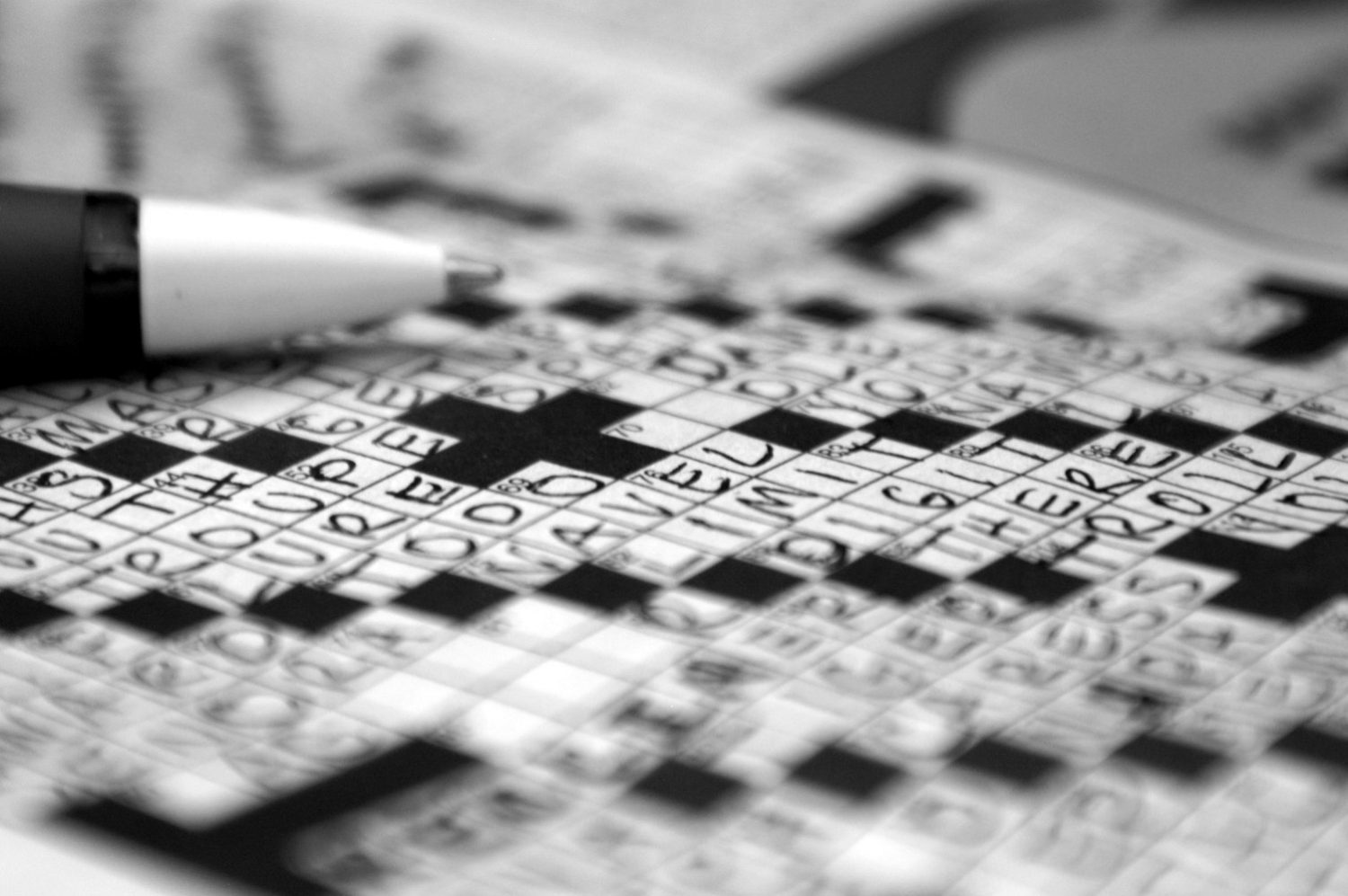 Close up of filled out crossword puzzle and tip of pen, in black and white