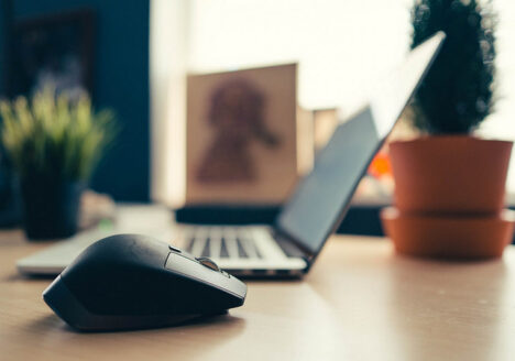 Soft focus laptop and plants in backround on table with computer mouse in foreground