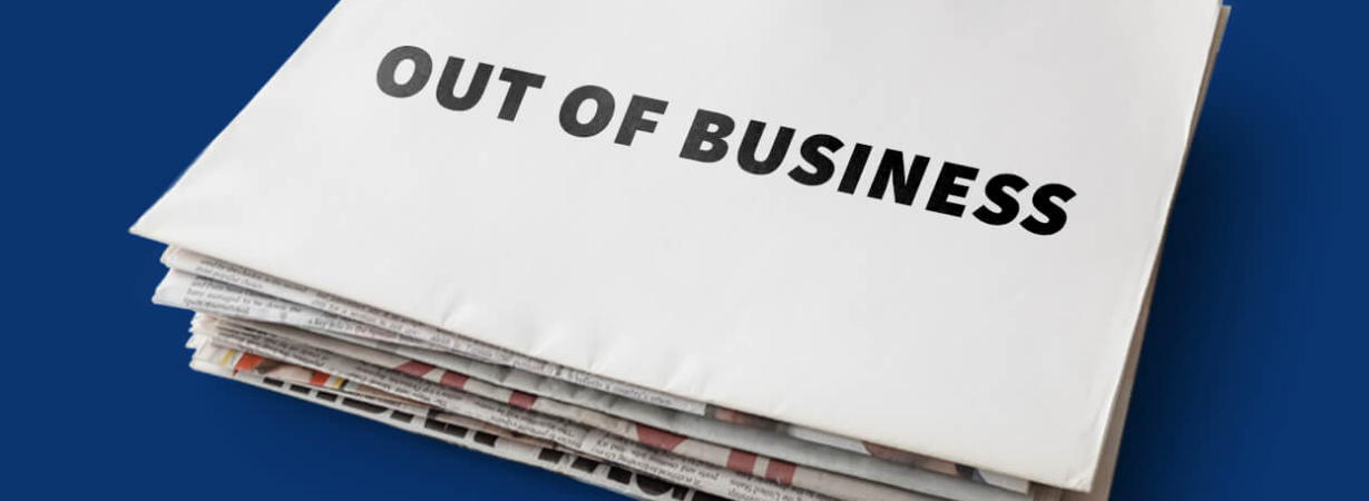 Stack of newspapers with blank sheet on top that says "Out of business" in all caps, black block letters, over dark blue background