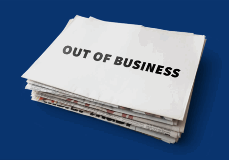 Stack of newspapers with blank sheet on top that says "Out of business" in all caps, black block letters, over dark blue background