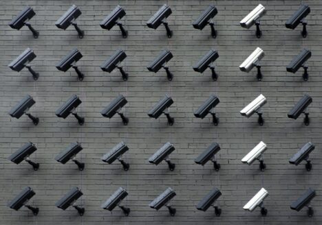 A brick wall of black and white surveillance cameras pointing down.