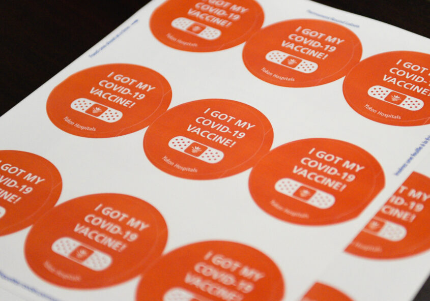 A sheet of 9 orange COVID-19 vaccination stickers on white paper, that say "I GOT MY COVID-19 VACCINE!" with a drawing of a bandaid underneath. Bottom reads "Yukon Hospitals"