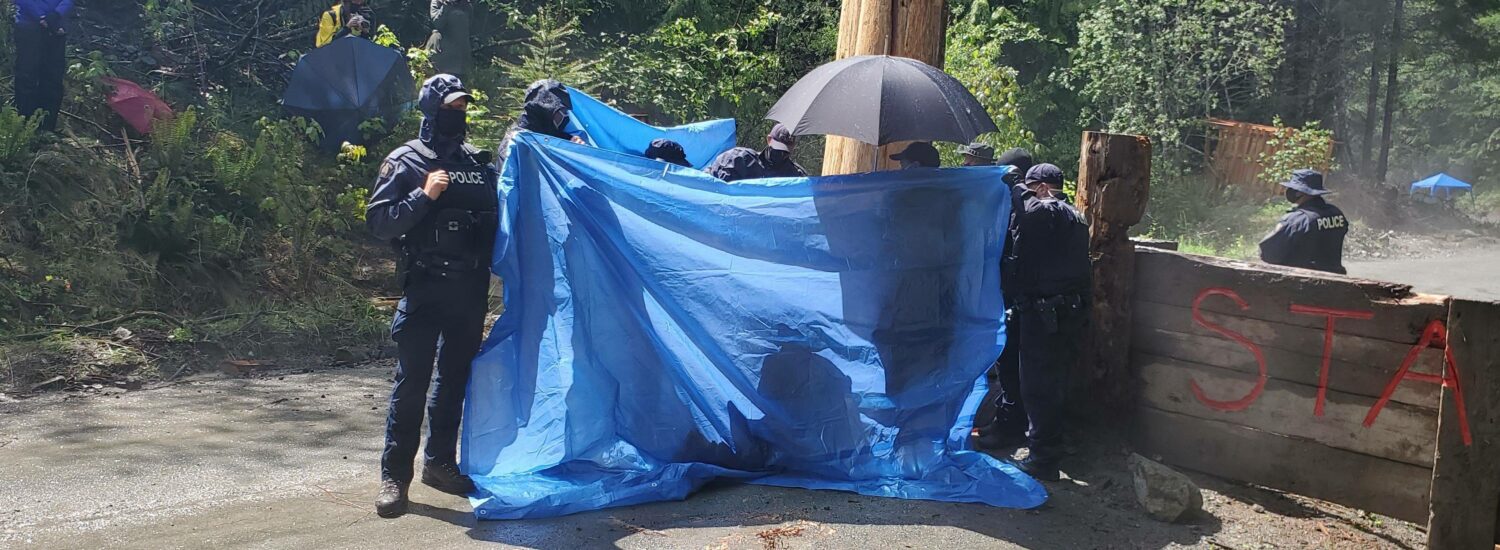 RCMP using tarps to obstruct media access as an arrest takes place last week.