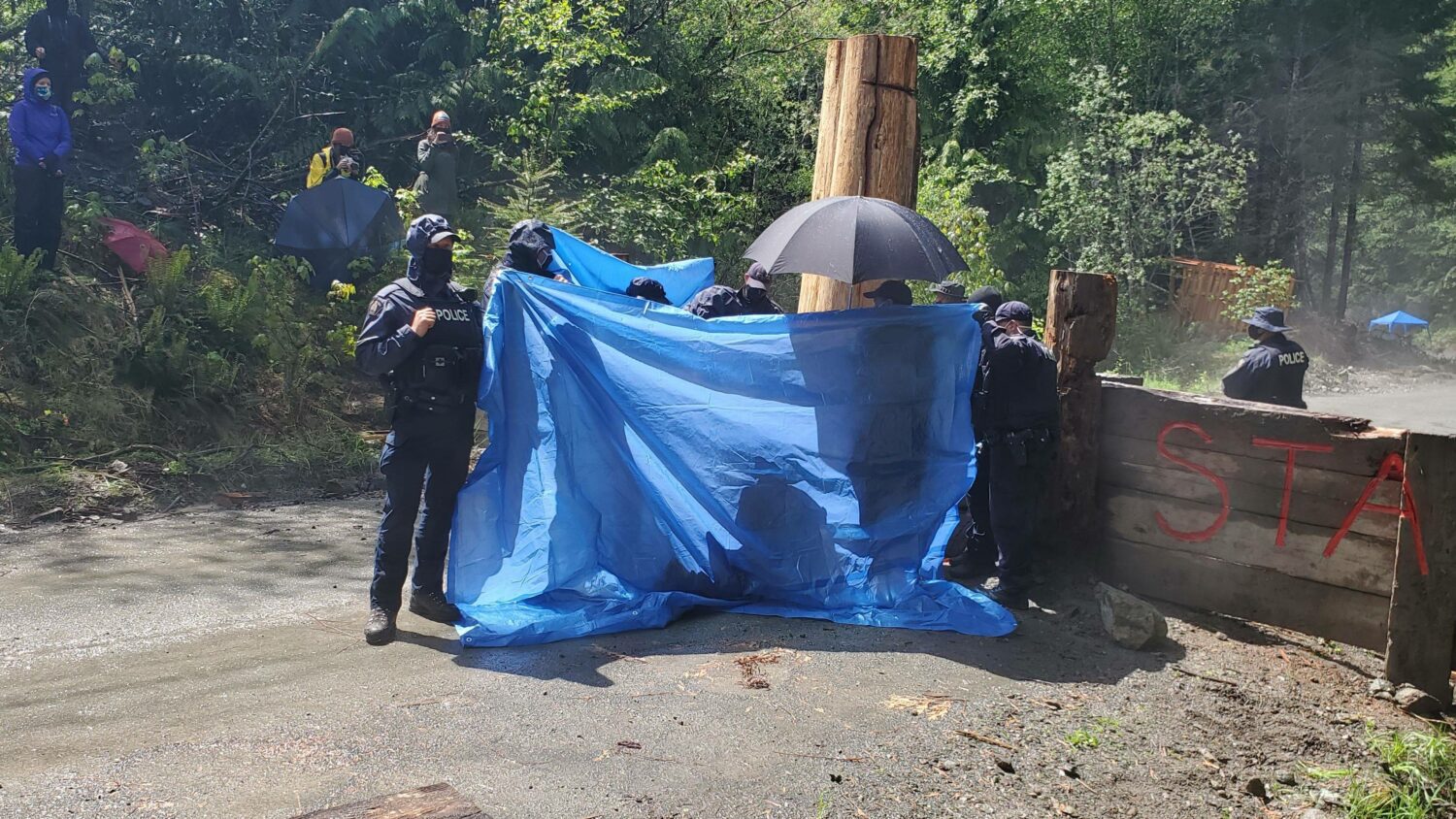 RCMP using tarps to obstruct media access as an arrest takes place last week.