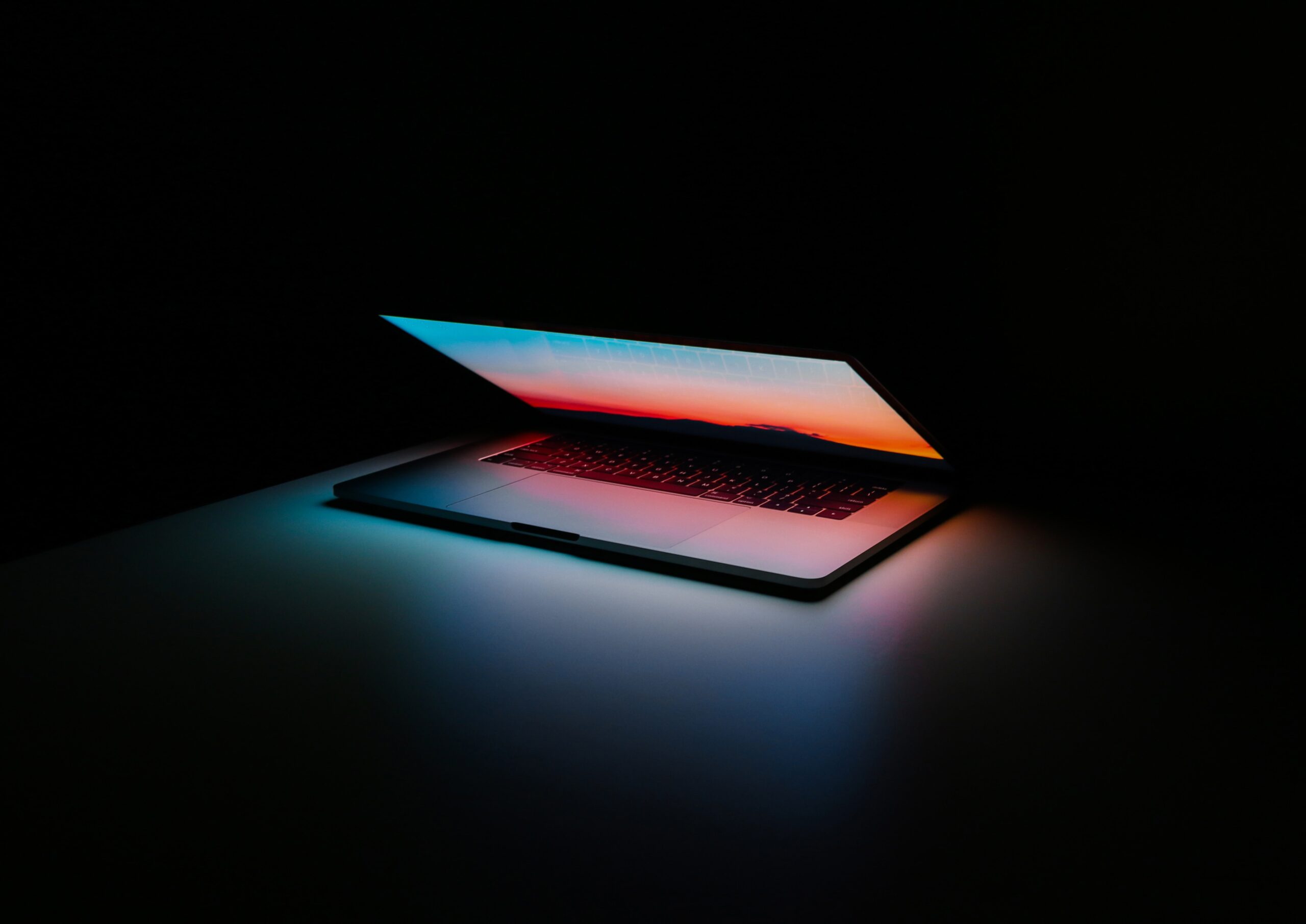 Partway opened laptop casting blue and orange light on a table in a dark room.