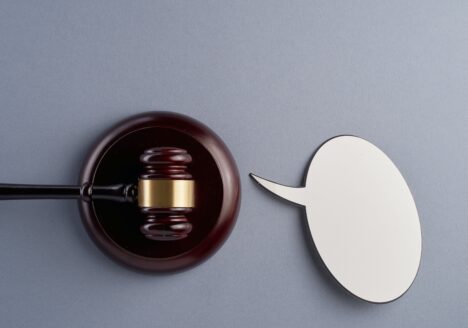 Gavel resting and white speech bubble cutout on light blue/gray background