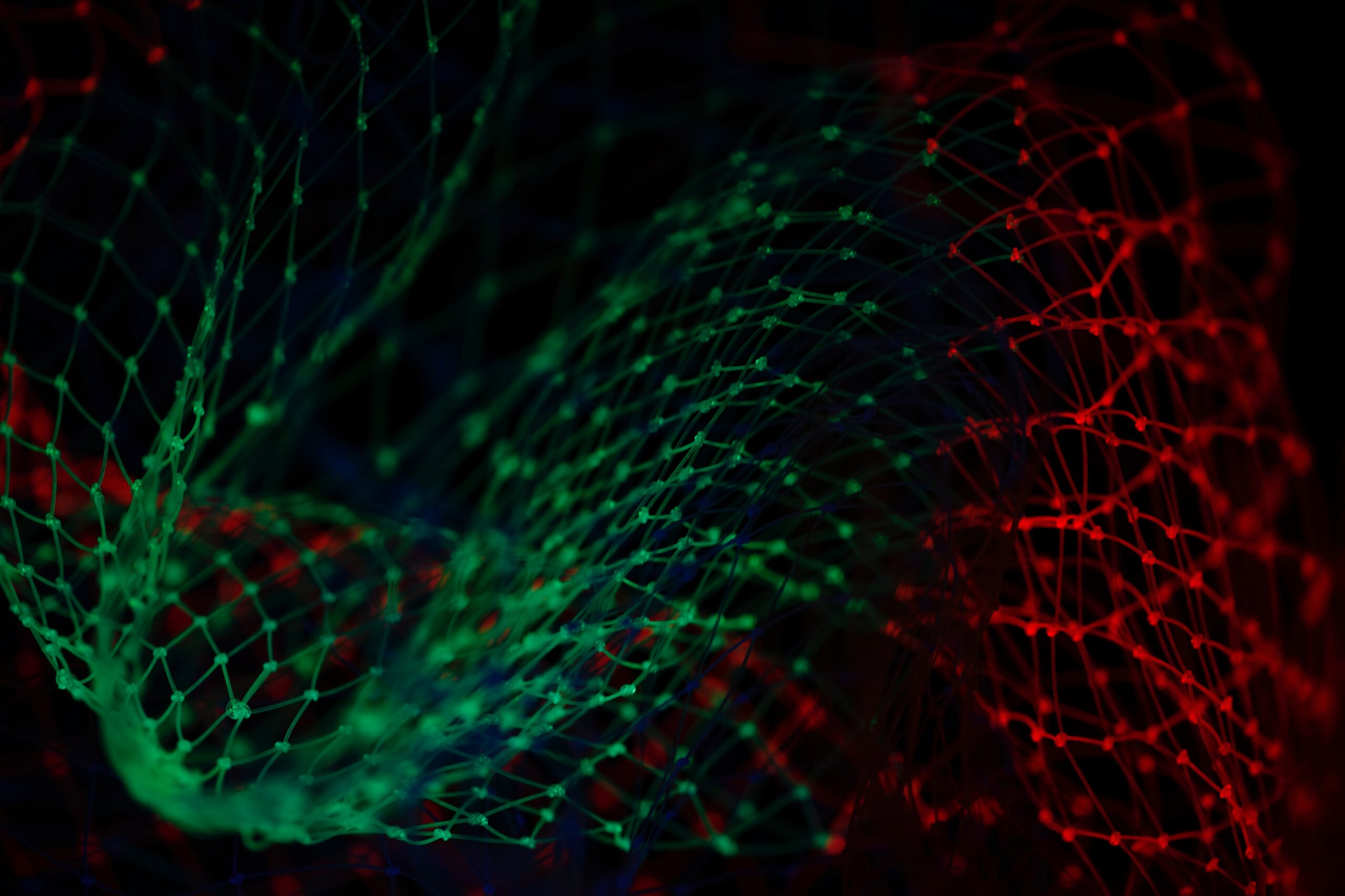 Green, red and blue light reflecting off netting over black background.