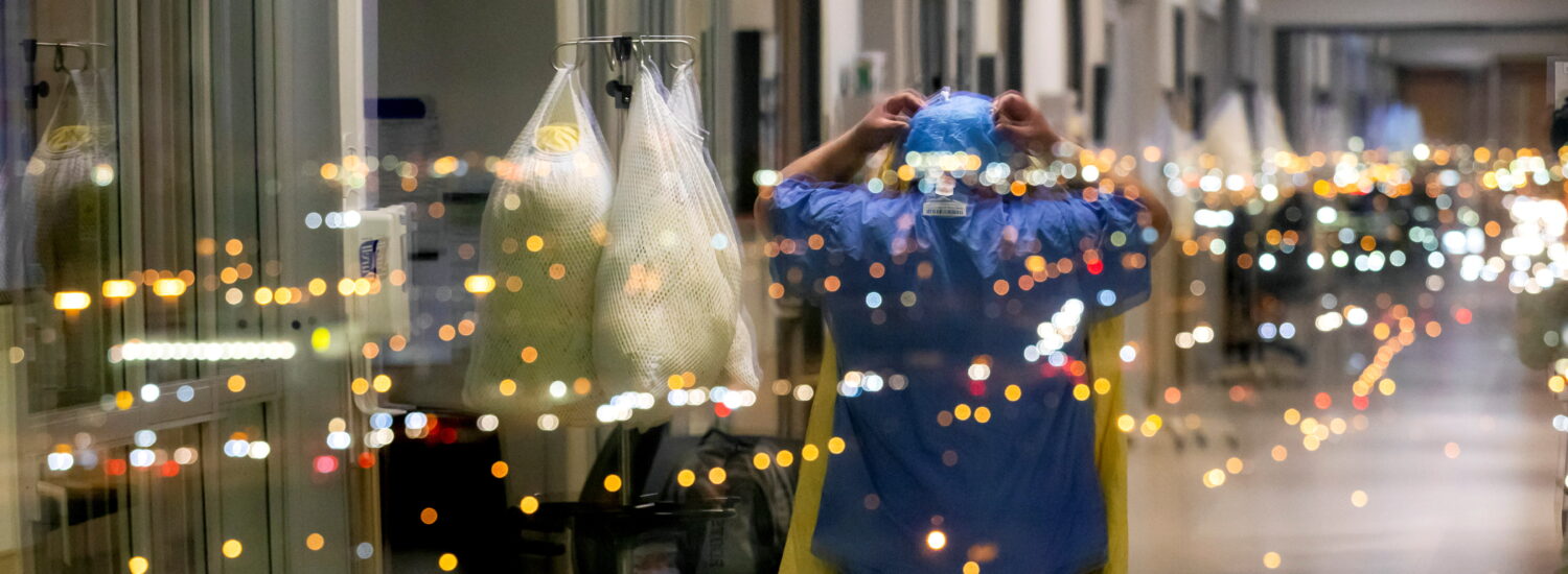 A nurse is reflected in a window as she puts on personal protective equipment to treat a COVID-19 patient inside the intensive care unit of Humber River Hospital in Toronto on April 20, 2021.