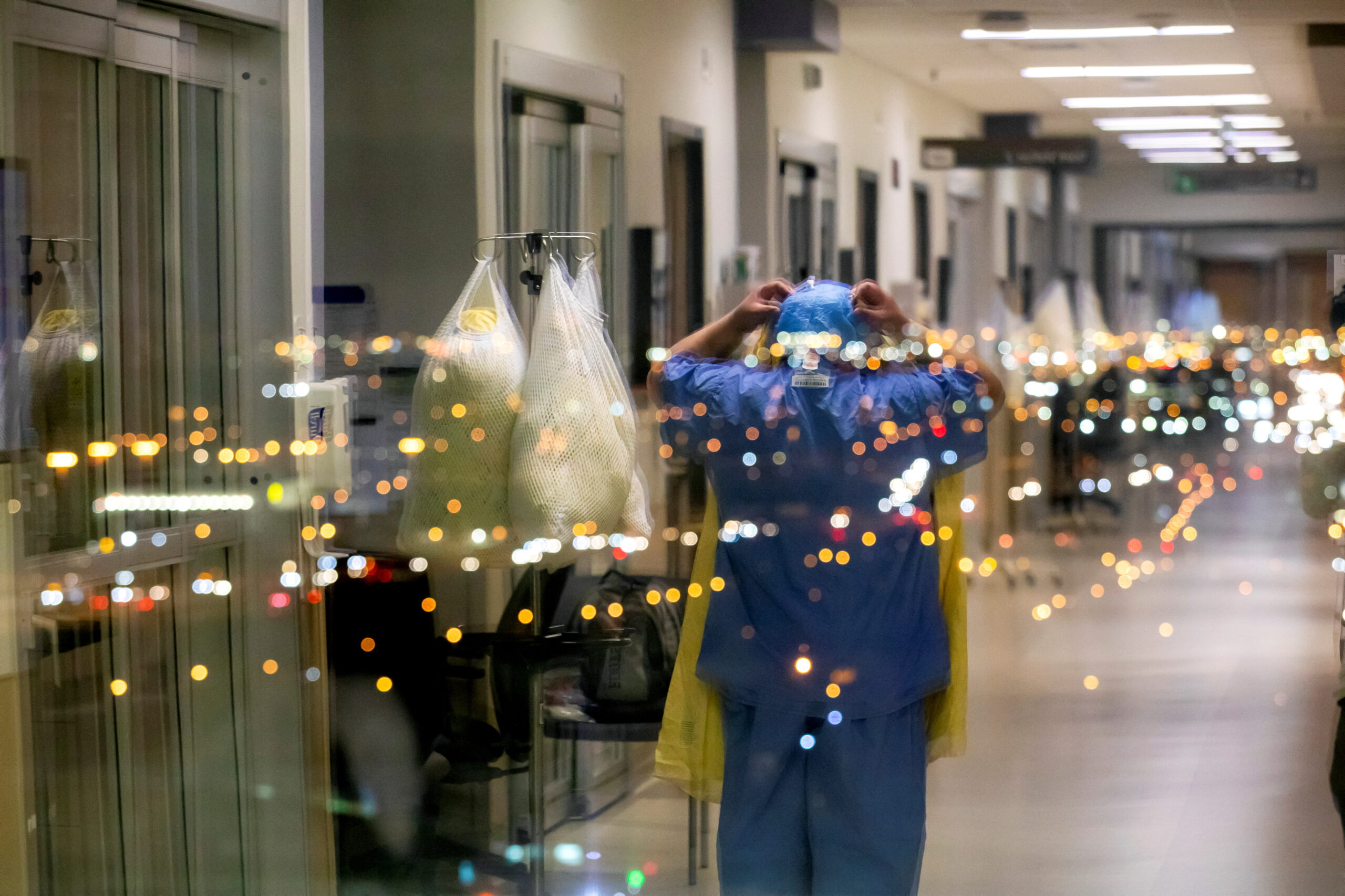 A nurse is reflected in a window as she puts on personal protective equipment to treat a COVID-19 patient inside the intensive care unit of Humber River Hospital in Toronto on April 20, 2021.