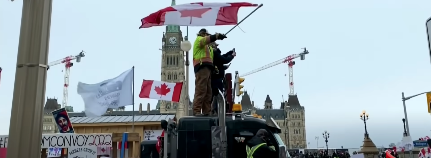Protesters waving nadian flag stand on top of and surrounding trucks in Ottawa