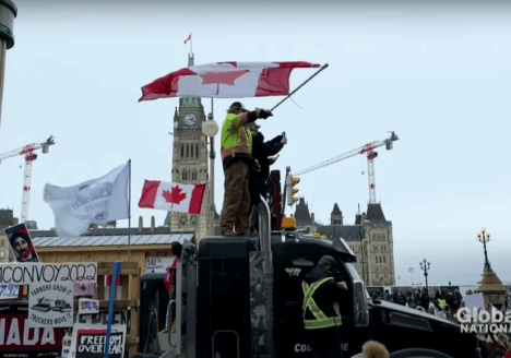 Protesters waving Canadian flag stand on top of and surrounding trucks in Ottawa