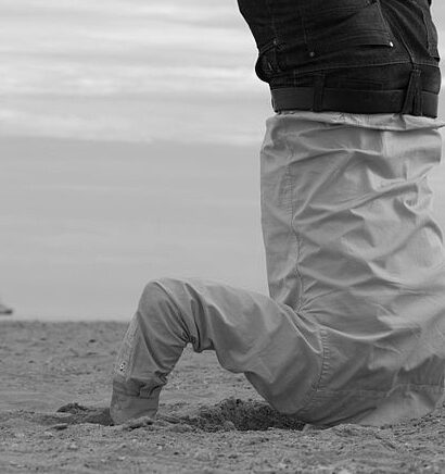 A person upside down with their head buried in sand on a beach. Photo in black and white