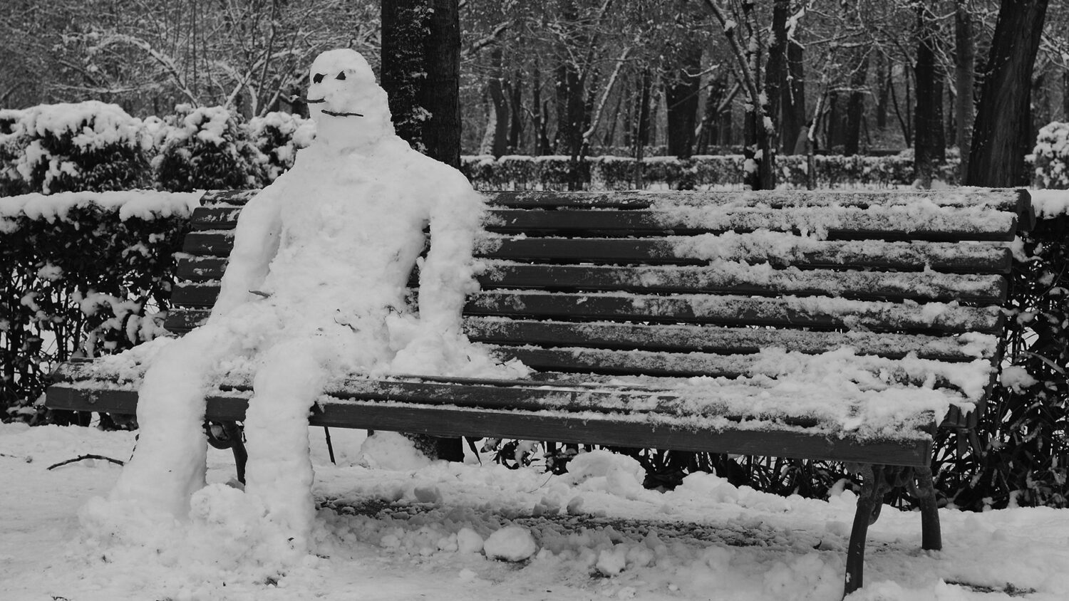 Snowman sitting on bench. Photo in black and white
