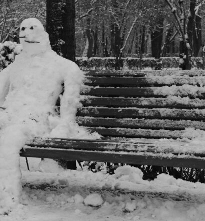 Snowman sitting on bench. Photo in black and white