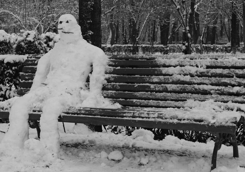 Snowman sitting on bench. Photo in black and white
