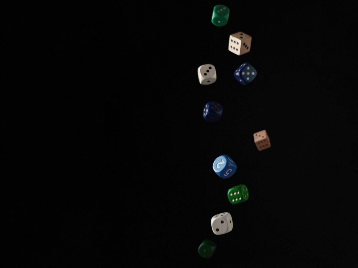 Multi-coloured dice falling in front of black background