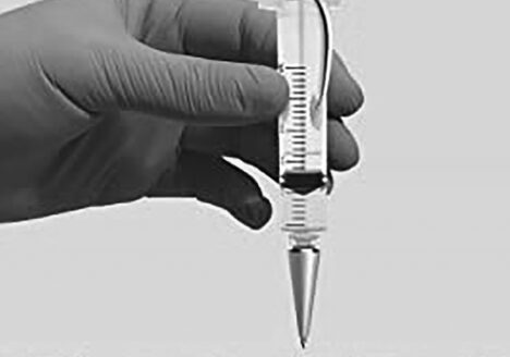 Gloved hand holds syringe vertically
