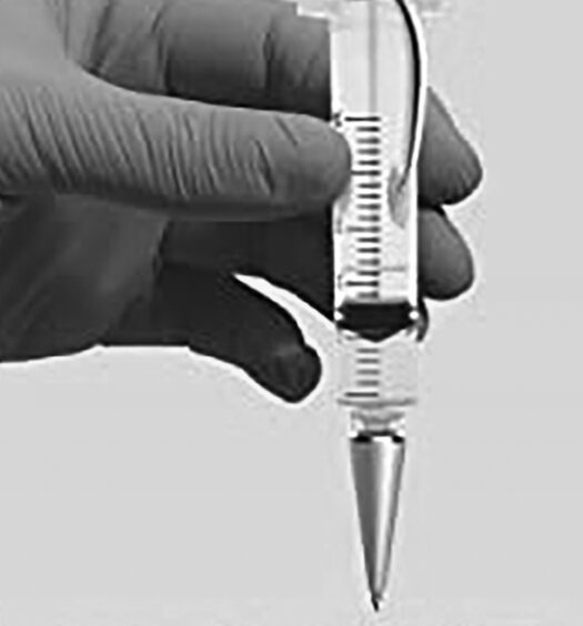 Gloved hand holds syringe vertically