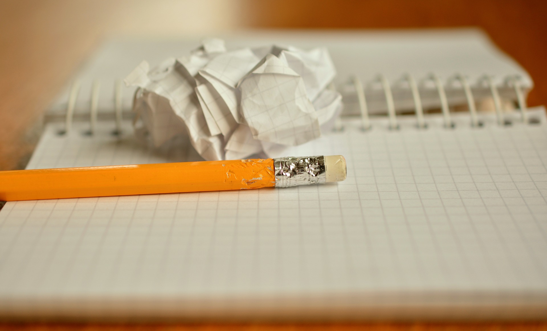 Pencil on notebook beside crumpled piece of paper