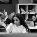 Four students work at laptops, one in foreground and three in background. Photo in black and white