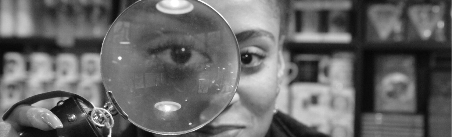Person staring straight ahead holding magnifying glass in front of right eye