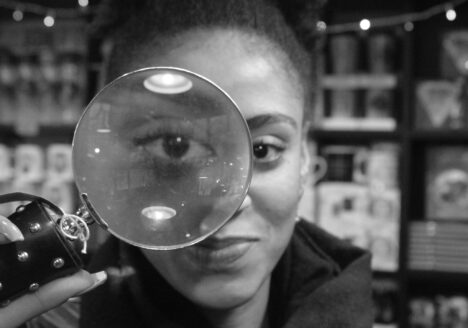 Person staring straight ahead holding magnifying glass in front of right eye