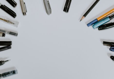 The tops of pens and pencils spanned around in a circle on a blank sheet of paper