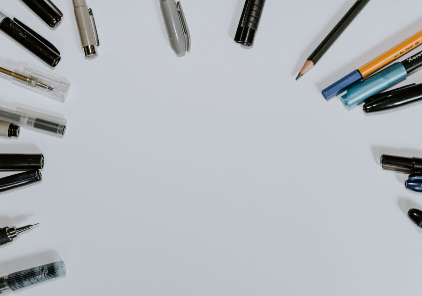 The tops of pens and pencils spanned around in a circle on a blank sheet of paper