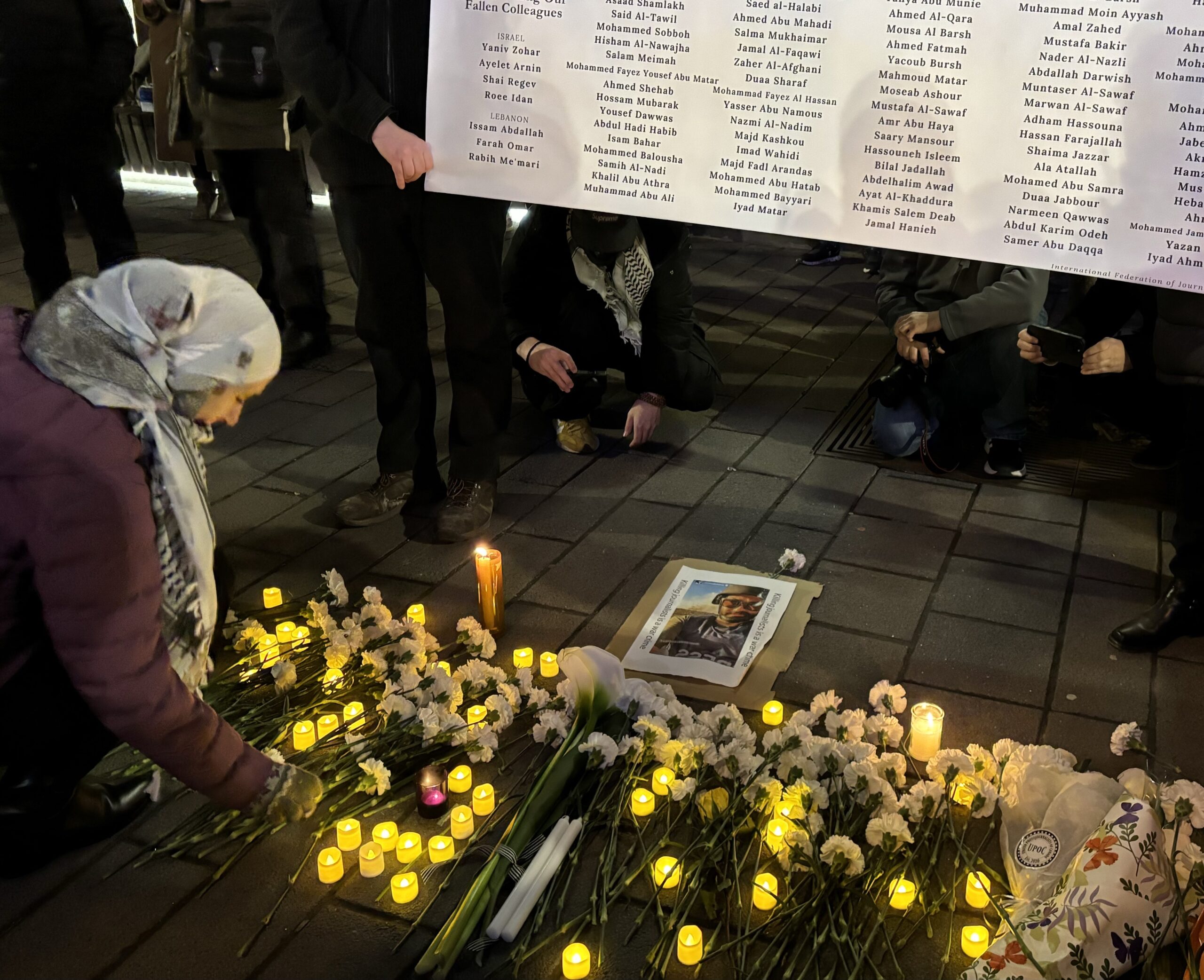 In this photo a woman is putting a flower down at a vigil for slain Palestininan, Lebanese and Israeli journalists. She is bending down in front of a poster carried by two people with all the journalists' names on it.