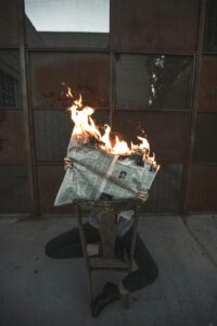 A newspaper on fire held in someone's hands