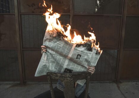 A newspaper on fire held in someone's hands