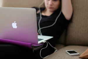 Person sitting back on couch with a computer on their lap and wearing headphones.