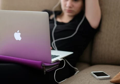 Person sitting back on couch with a computer on their lap and wearing headphones.