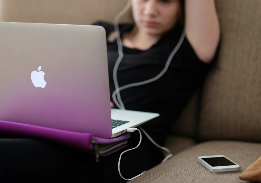 Person sitting back on couch with a computer on their lap and wearing headphones.