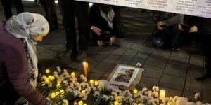 In this photo a woman is putting a flower down at a vigil for slain Palestininan, Lebanese and Israeli journalists. She is bending down in front of a poster carried by two people with all the journalists' names on it.