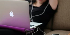 Person sitting back on couch with a computer on their lap and wearing headphones.