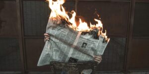 A newspaper on fire held in someone's hands