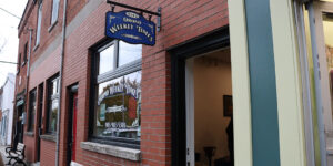 Exterior of the Orono Weekly Times. Brick facade with window and blue sign.